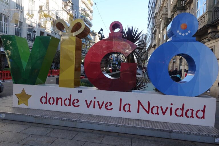 De grandes lettres colorées formant le mot Vigo en forme de cadeau, de boule et de bonhomme de neige, au-dessus de l’inscription « donde vive la Navidad », dans une rue du centre