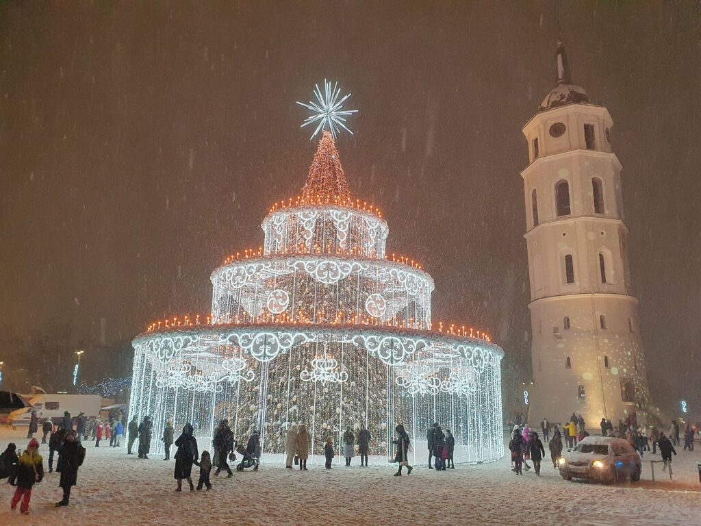 Le sapin lumineux à étages de la place de la Cathédrale de Vilnius sous la neige, à côté du campanile, de nuit